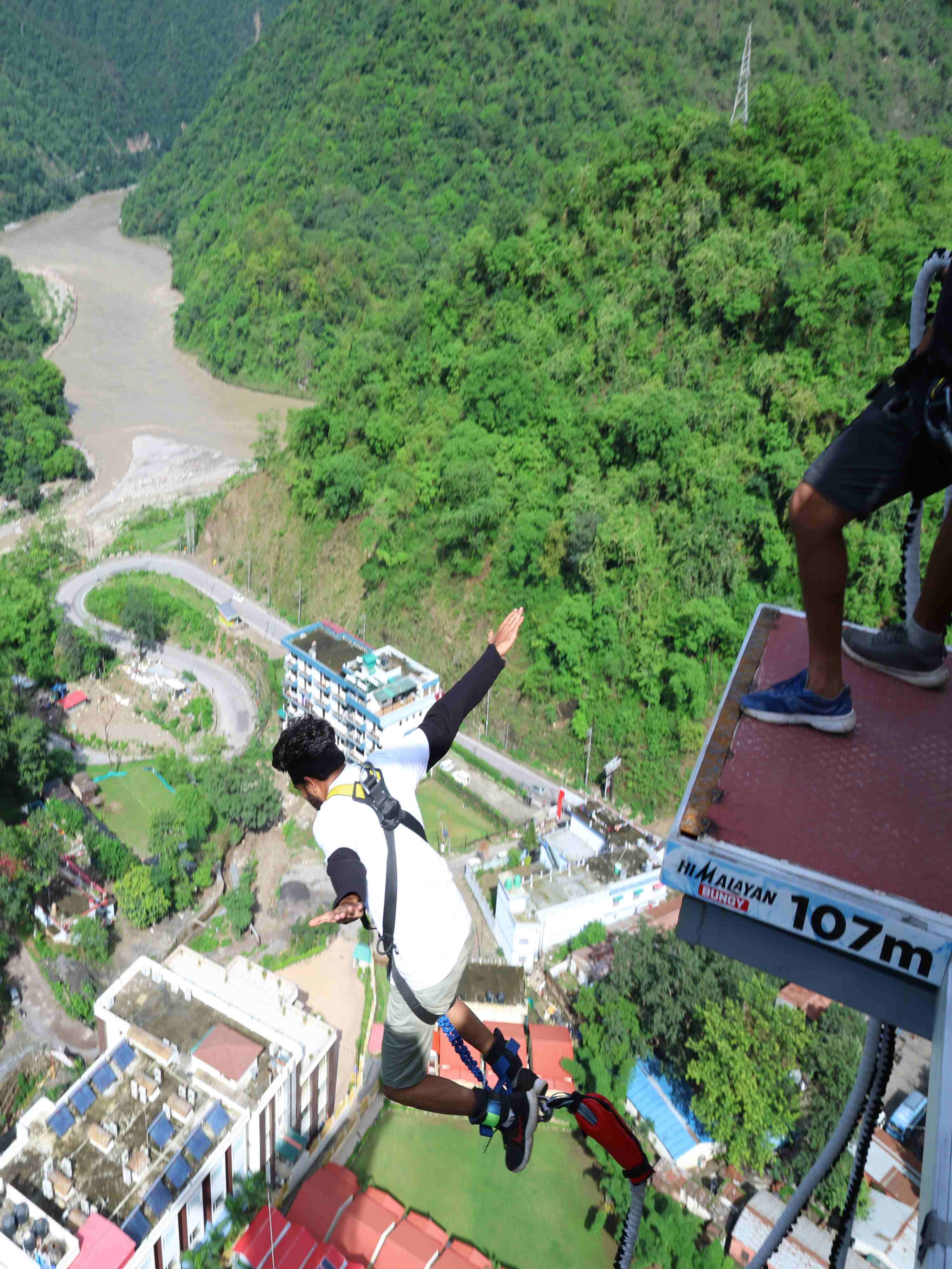 Adventurer preparing for the bungee jump with instructors gearing up and capturing photos at the edge of the platform